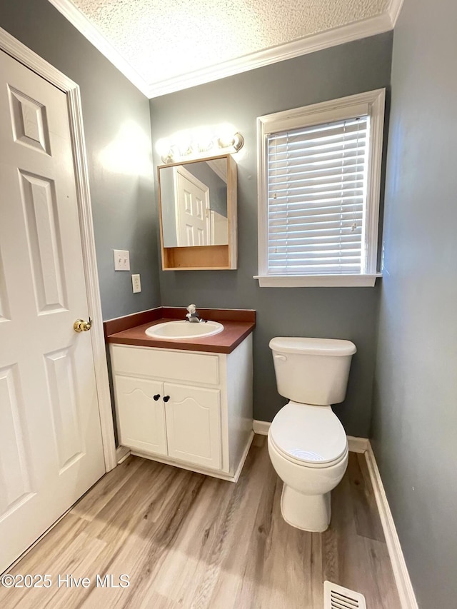 half bathroom featuring visible vents, toilet, wood finished floors, crown molding, and vanity