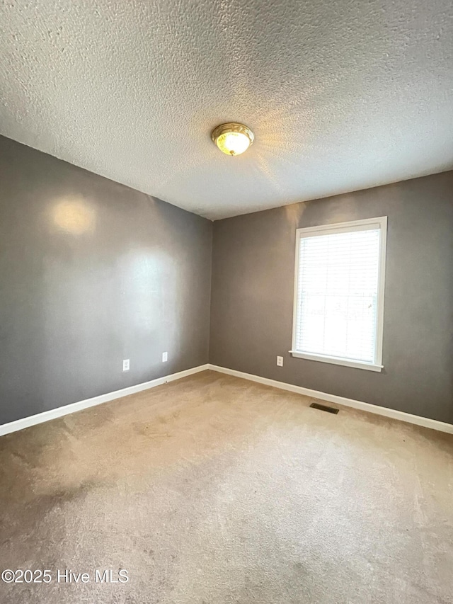 carpeted spare room with a textured ceiling, visible vents, and baseboards