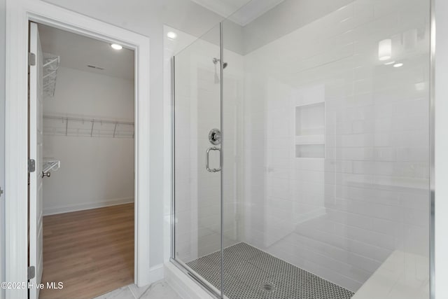 full bath featuring wood finished floors, a stall shower, a walk in closet, and baseboards