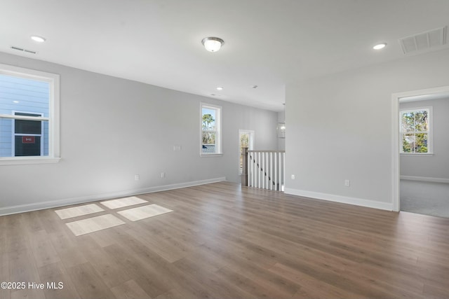 unfurnished room with baseboards, wood finished floors, visible vents, and a healthy amount of sunlight