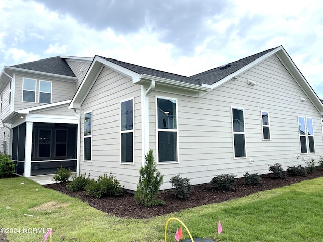 view of side of home with a sunroom, roof with shingles, and a lawn