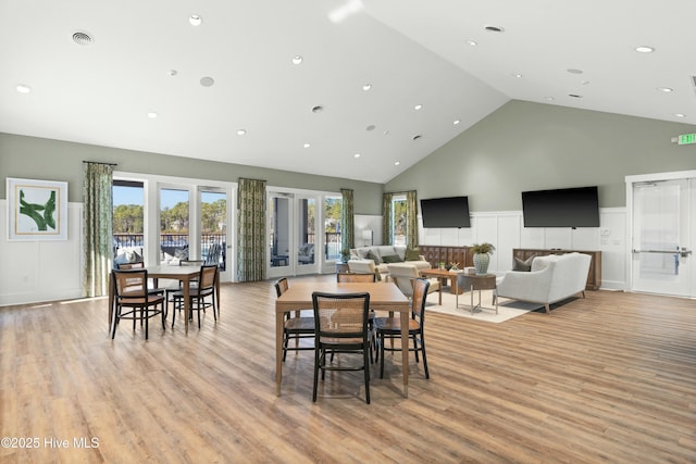 dining area featuring high vaulted ceiling, light wood-type flooring, a wainscoted wall, and visible vents