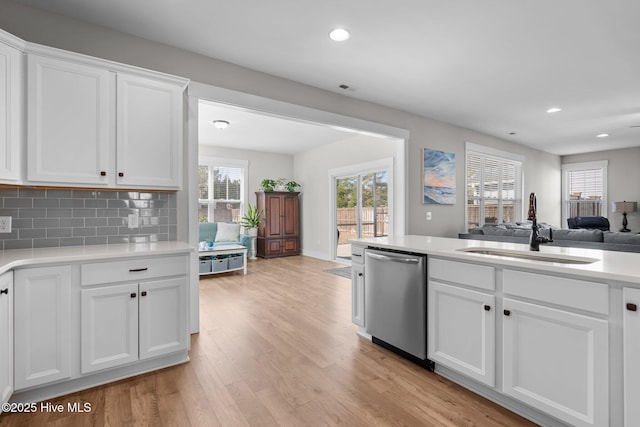 kitchen with light wood finished floors, open floor plan, light countertops, stainless steel dishwasher, and a sink