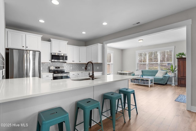 kitchen with light wood finished floors, visible vents, decorative backsplash, appliances with stainless steel finishes, and a sink