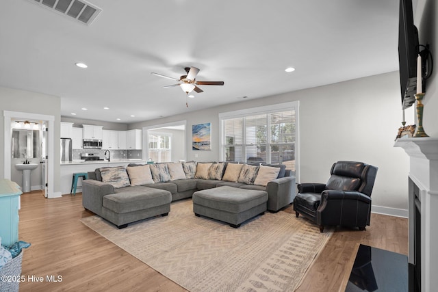 living room featuring light wood-style flooring, a fireplace with flush hearth, visible vents, and recessed lighting