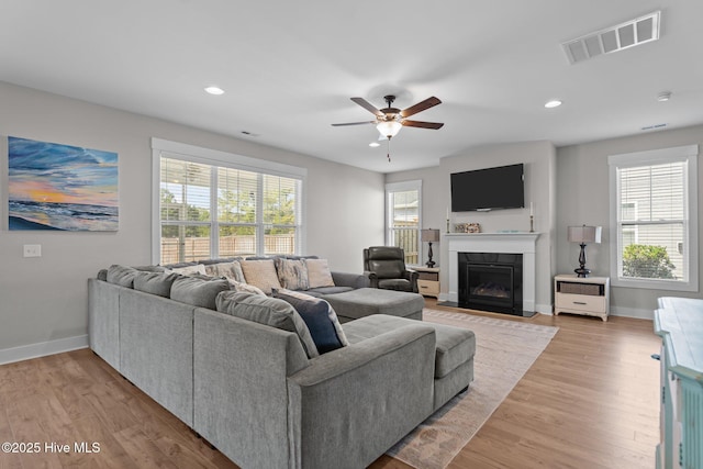 living room with baseboards, a fireplace with flush hearth, visible vents, and light wood-style floors