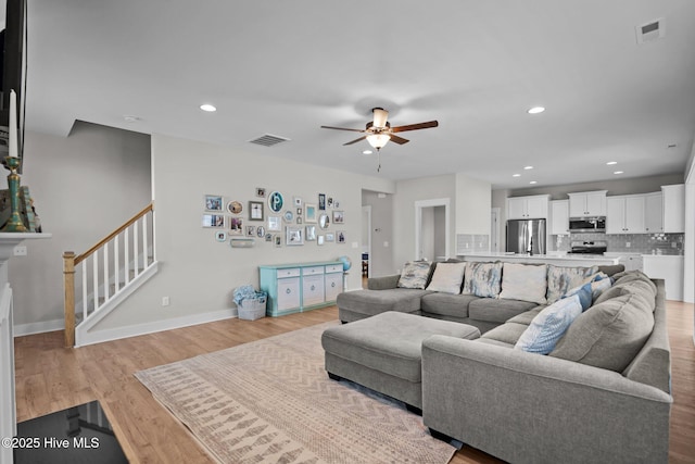 living area with recessed lighting, visible vents, light wood-style flooring, and stairs