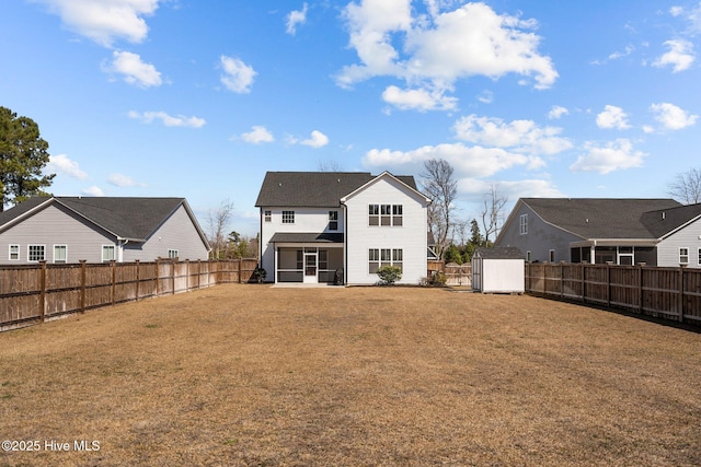 back of house with a sunroom, a fenced backyard, an outbuilding, a yard, and a shed