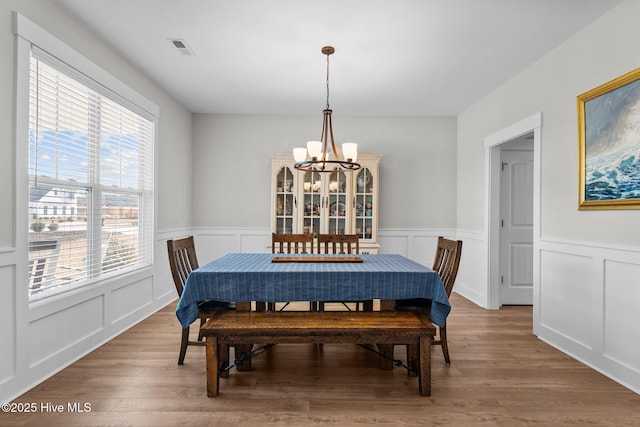 dining space with visible vents, a notable chandelier, a decorative wall, and wood finished floors