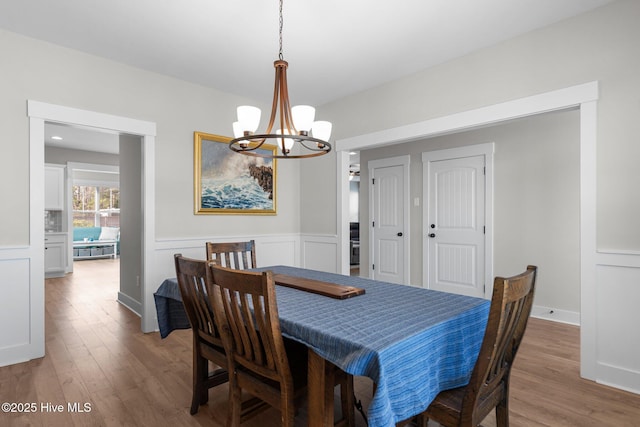 dining area featuring a wainscoted wall, a notable chandelier, a decorative wall, and wood finished floors