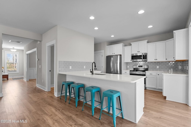 kitchen featuring a peninsula, stainless steel appliances, light wood-type flooring, a kitchen bar, and a sink