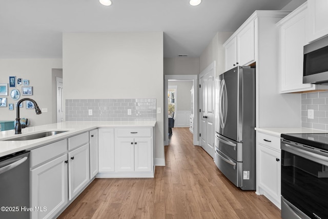 kitchen featuring stainless steel appliances, light countertops, light wood-style flooring, white cabinets, and a sink