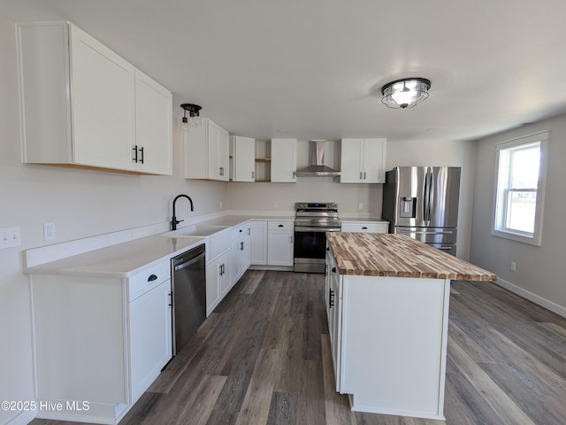 kitchen featuring butcher block countertops, a center island, stainless steel appliances, wall chimney range hood, and a sink