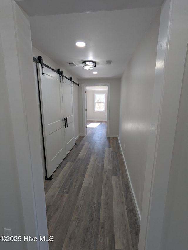 corridor featuring baseboards, a barn door, visible vents, and wood finished floors