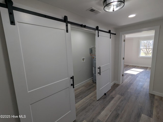 corridor featuring a barn door, wood finished floors, visible vents, and baseboards