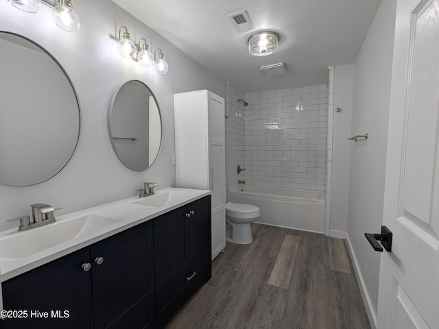 bathroom featuring toilet, wood finished floors, a sink, and visible vents