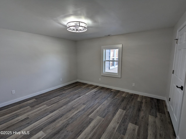 spare room with dark wood-style floors, visible vents, and baseboards