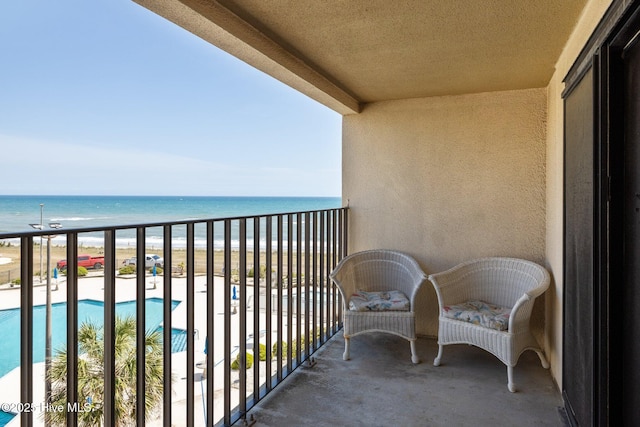 balcony with view of water and beach and view of pool area