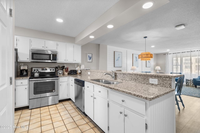 kitchen with stainless steel appliances, a peninsula, a textured ceiling, a sink, and recessed lighting