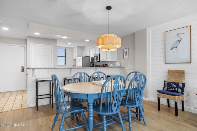 dining space with a textured ceiling, light wood finished floors, wood walls, and recessed lighting