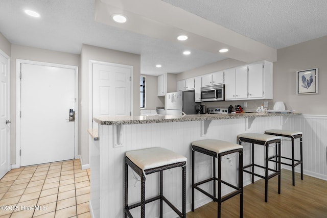 kitchen featuring appliances with stainless steel finishes, a peninsula, white cabinetry, recessed lighting, and a breakfast bar area