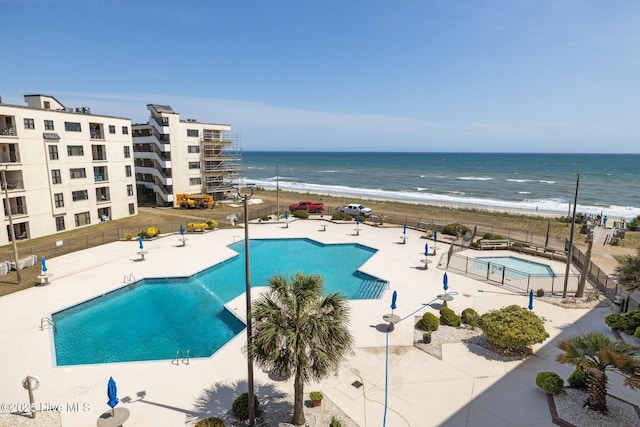 community pool with fence, a patio area, and view of water and beach