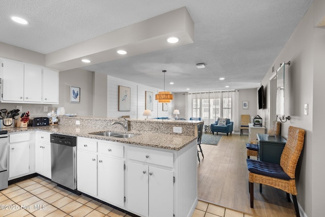 kitchen featuring stainless steel appliances, a sink, a peninsula, open floor plan, and white cabinets