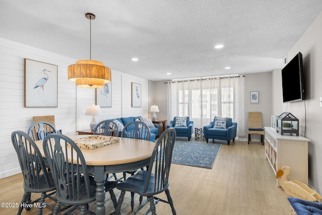 dining area with a textured ceiling, light wood finished floors, recessed lighting, wood walls, and baseboards