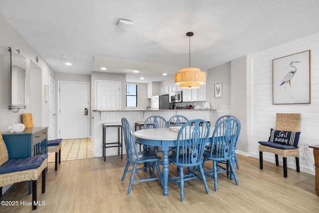 dining room featuring light wood finished floors, a textured ceiling, and recessed lighting