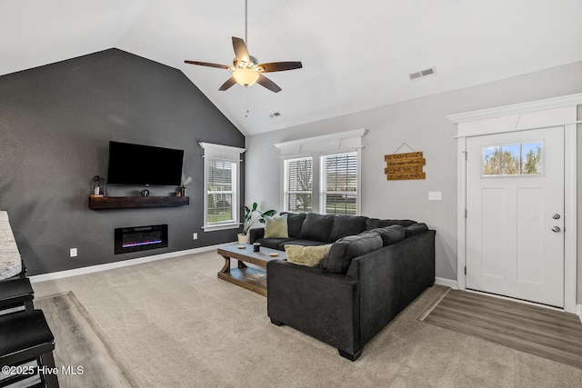 carpeted living area featuring visible vents, a ceiling fan, a glass covered fireplace, vaulted ceiling, and baseboards