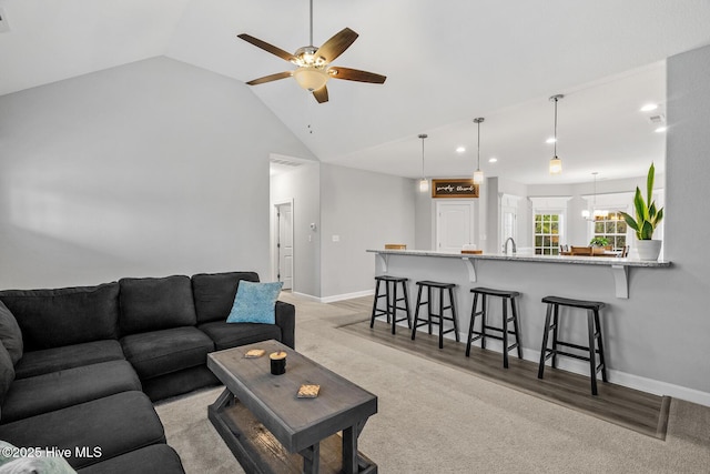 living area featuring vaulted ceiling, light wood finished floors, ceiling fan with notable chandelier, and baseboards