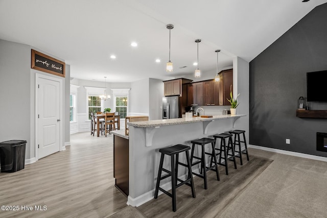 kitchen featuring a breakfast bar, stainless steel refrigerator with ice dispenser, dark brown cabinetry, light stone countertops, and a peninsula