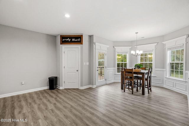 dining space with an inviting chandelier, a decorative wall, wood finished floors, and wainscoting