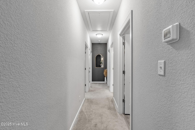 corridor with light carpet, attic access, and a textured wall