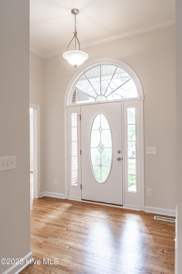 entrance foyer with crown molding, baseboards, light wood-type flooring, and visible vents