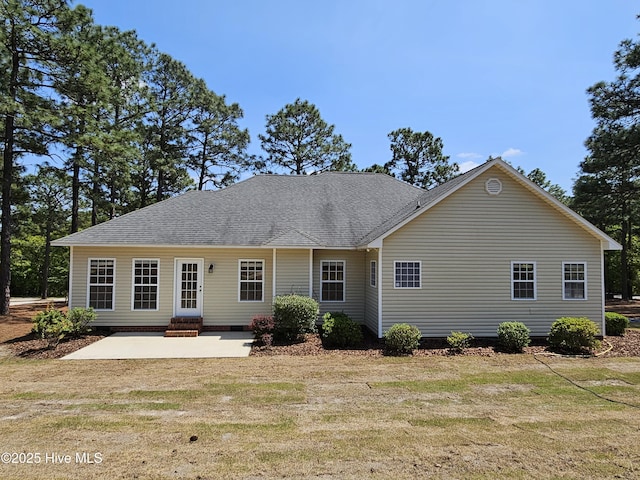 back of property with a lawn, a patio, a shingled roof, and crawl space