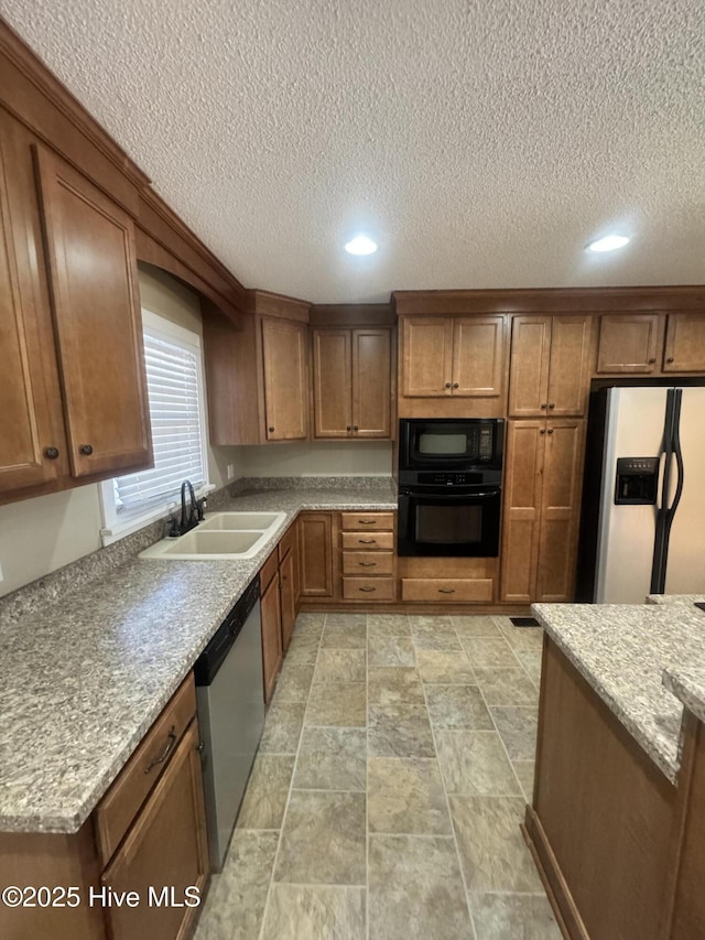 kitchen with black appliances, light stone counters, brown cabinetry, and a sink