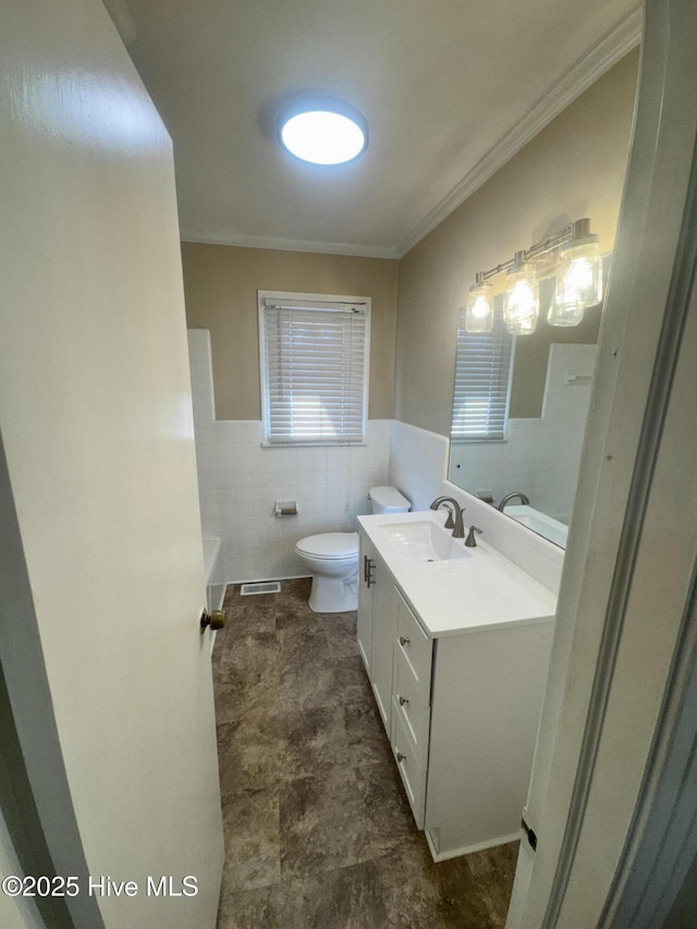 full bath featuring crown molding, tile walls, toilet, wainscoting, and vanity