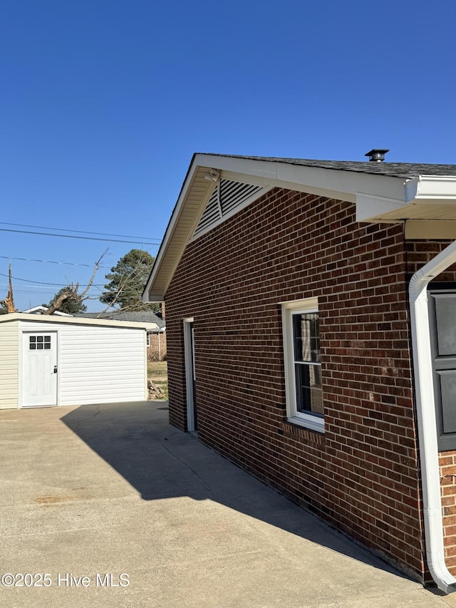 view of side of property with concrete driveway, brick siding, and an outdoor structure