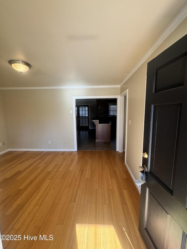 unfurnished living room with baseboards, crown molding, and light wood finished floors