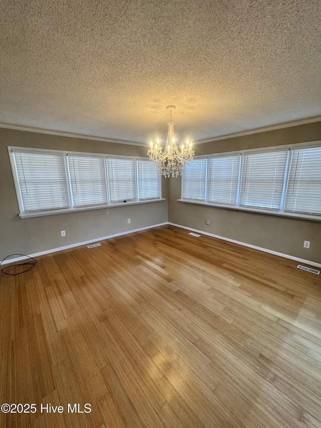 spare room featuring visible vents, a textured ceiling, an inviting chandelier, and wood finished floors