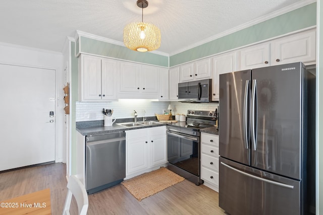 kitchen with light wood finished floors, stainless steel appliances, dark countertops, white cabinets, and a sink