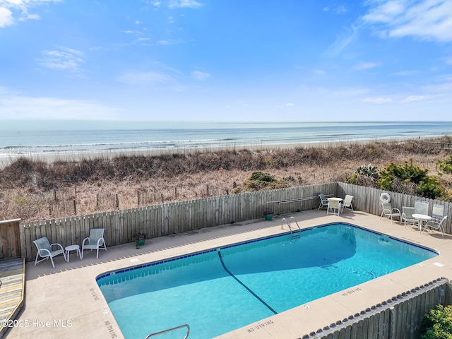 community pool featuring a water view, fence, a patio, and a view of the beach