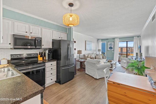 kitchen with appliances with stainless steel finishes, light wood-style floors, open floor plan, white cabinetry, and ornamental molding