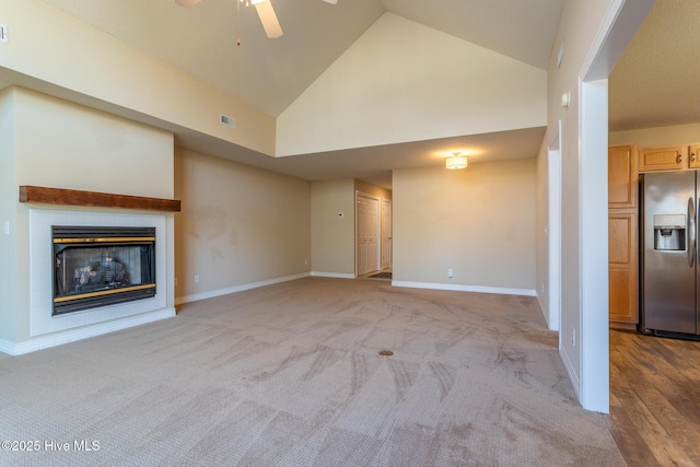 unfurnished living room with high vaulted ceiling, light carpet, visible vents, baseboards, and a glass covered fireplace