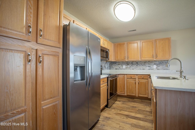 kitchen featuring a textured ceiling, wood finished floors, a sink, appliances with stainless steel finishes, and tasteful backsplash