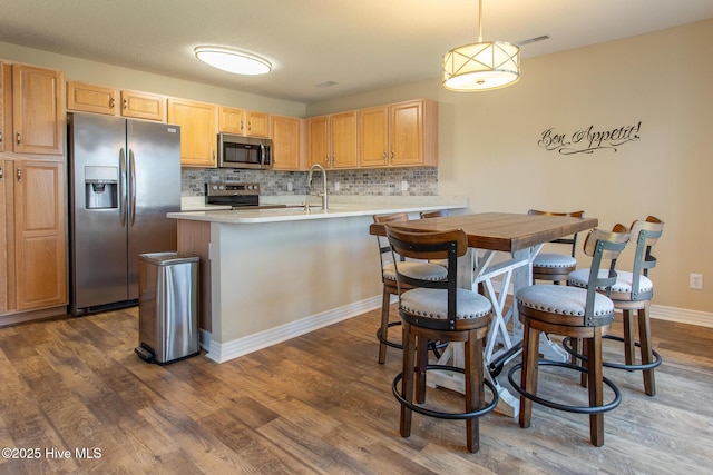 kitchen featuring dark wood finished floors, stainless steel appliances, tasteful backsplash, light countertops, and light brown cabinets