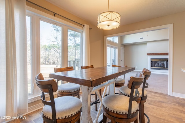 dining area with light wood-type flooring, a glass covered fireplace, and baseboards