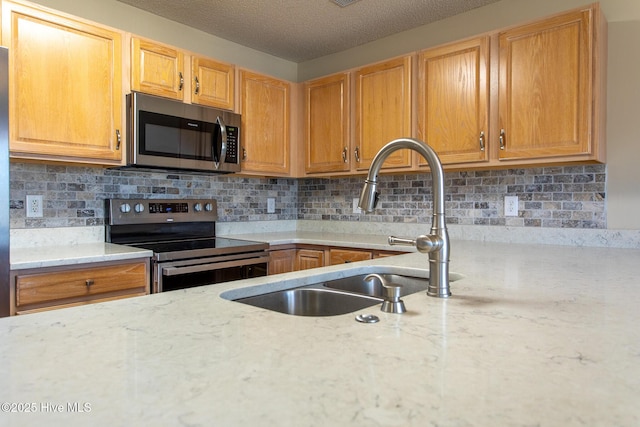 kitchen with backsplash, light stone counters, stainless steel appliances, and a sink