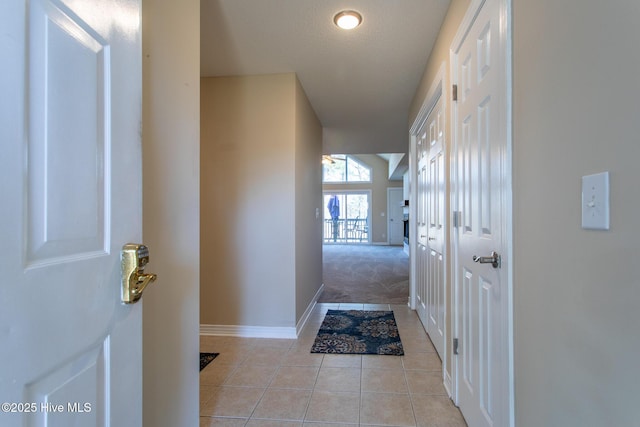 hall with light carpet, light tile patterned floors, and baseboards